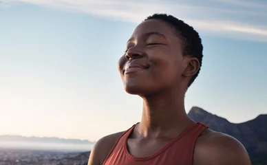 Tuinposter Fitness, calm and breathing of black woman outdoor in nature, mountains and blue sky background for yoga wellness, meditation and zen energy. Face of girl breathing for peace, freedom and mindfulness © C Malambo/peopleimages.com