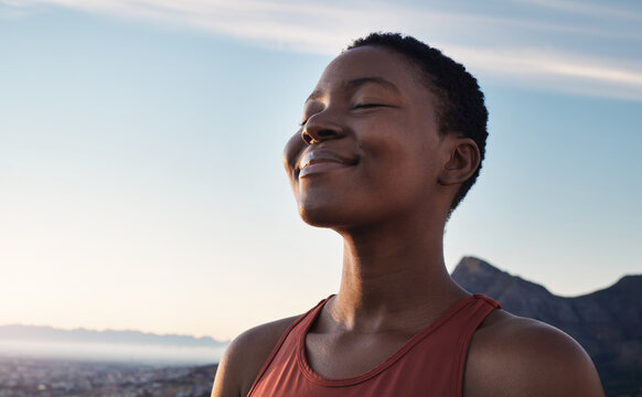Fitness, calm and breathing of black woman outdoor in nature, mountains and blue sky background for yoga wellness, meditation and zen energy. Face of girl breathing for peace, freedom and mindfulness