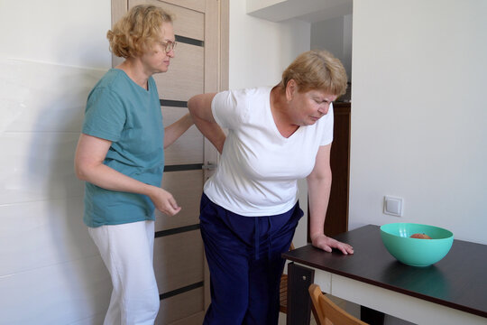 Nurse Helps Over Weight Blond Middle-aged Woman Suffering From Back Ache On The Kitchen, Healthcare And Problem, Woman Rubbing Aching Back