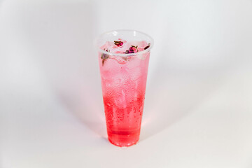 Pink lemonade with ice and pink rose buds in a transparent glass on a white background.