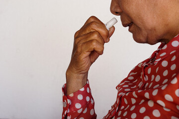 Closeup Asian woman use inhaler to smell  for relieve dizzy or faint symptoms. Concept, health problem, sickness and remedy. Increases freshness, reduces dizziness and stuffy nose. self take care.    - obrazy, fototapety, plakaty