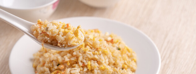 Eating Chinese fried rice in white plate on bright wooden table background.