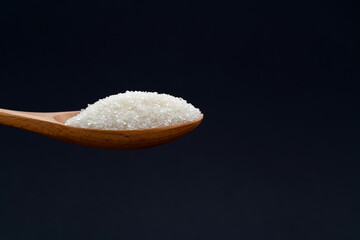 Wooden spoon with sugar crystals on black background