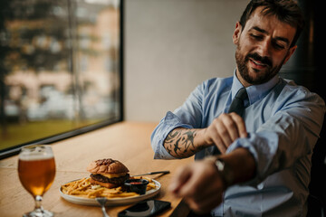 Attractive businessman rolling up his sleeves on his shirt, preparing for relaxation with a beer and burger.