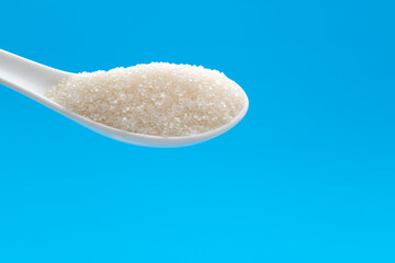 Ceramic spoon with sugar crystals on blue background