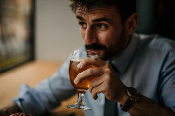 Close up image of a successful businessman holding a beer glass, looking aside with a proud face, and about to drink it.