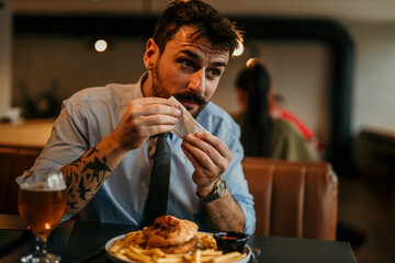 Good looking businessman using a napkin while having a burger, beer, and french fries for a lunch.