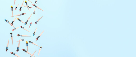 Diverse paint brushes falling, empty blue background