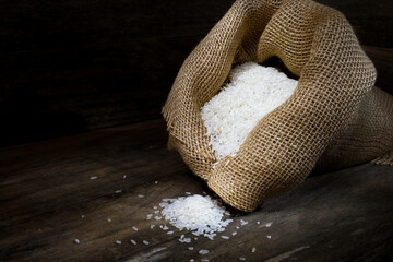 Fototapeta na wymiar A rustic scene of a hessian bag overflowing with long grain White Rice on a wooden box-like surrounding in dark mood lighting; captured in a Studio