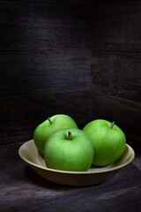 Rustic scene three green Granny Smith apples yellow bowl wooden box surroundings dark mood lighting