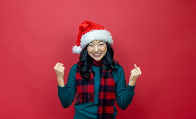 Pretty smiling asian woman in warm christmas sweater and santa hat is having excitement on red background for season celebration concept with copy space