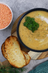 red lentils soup puree in dark bowl with bread on grey marble table