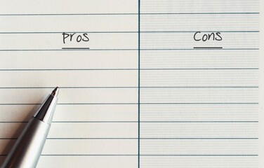 A silver pen on a line note paper with two choices to choose between PROS and  CONS - concept of...