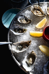 Oysters on metal tray with ice, lemon Restaurant menu, dieting, cookbook recipe. Expensive meal. Healthy food, gourmet, raw sea ocean. professional chef cooks set seafood sauce Cooking mediterranean