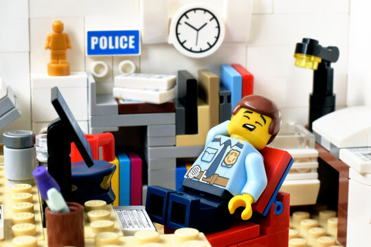Lego minifigure of police officer is sleeping in the office. Editorial illustrative image of law and punishing. Studio shot.