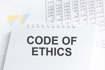 CODE OF ETHICS is written on a white card next to a potted flower, diaries and calculator. Organizational concept
