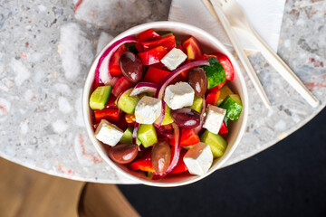 Diet Greek salad with feta, tomatoes, greens on a gray stone background top view. Healthy lunch.