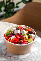 Diet Greek salad with feta, tomatoes, greens. Healthy lunch. Food delivery in disposable plate of craft paper.