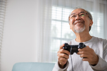 Asian senior old man enjoying holding joystick playing video game at home in living room, mature man hands using game controller, Funny on retirement elderly smile sitting on sofa life gaming