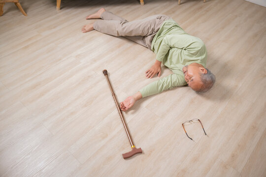 Asian elderly man retired headache after fall down, Sick senior old man falling down lying on floor at house alone with wooden cane walking stick in living room, Health care and medicine concept
