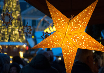 Von Innen beleuchteter gelber Stern vor Weihnachtsmarkt