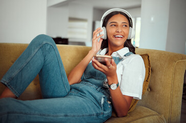 Young girl, headphones and music with smartphone, relax at home with technology and listening to podcast, radio and audio streaming. Online, social network and happy on sofa with sound and wellness.