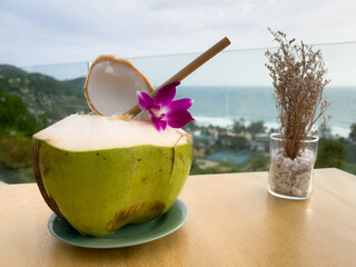 Fresh green coconut on restaurant table with great views of Kata Noi beach in Phuket, Thailand. Summer vacation leisure moment, travel destination concepts
