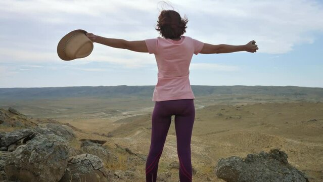 Woman with hat on the top of the hill with raised arms. 4k footage UHD 3840x2160