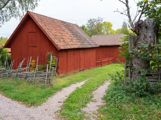A typically red wooden cottage and barn in a Swedish summer landscape