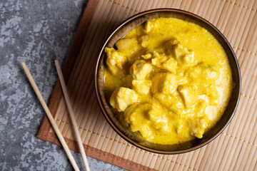 Chicken in curry sauce in a bowl on a bamboo napkin with chopsticks on a gray background