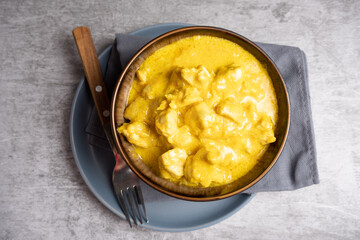 Chicken cooked in curry sauce in a bowl on a blue plate with a fork. Top view