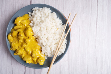 Boiled rice with chicken in curry sauce on a blue plate on a light background.