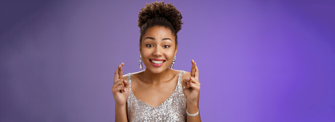Cheerful optimistic charming african american girlfriend supporting friend make wish wanna win first prize cross fingers luck smiling broadly wear glittering silver dress anticipating good fortune - obrazy, fototapety, plakaty