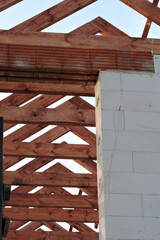 A timber roof truss in a house under construction, walls made of autoclaved aerated concrete blocks, a rough window opening, a reinforced brick lintel, blue sky in the background