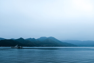 A boat on the calm sea with mountains as the background under cloudy weather