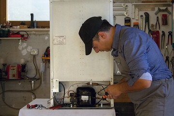 Appliance service technician in his workshop repairing a faulty refrigerator. Technician at work in the workshop.
