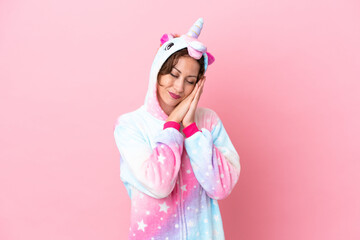 Young caucasian woman with unicorn pajamas isolated on pink background making sleep gesture in dorable expression