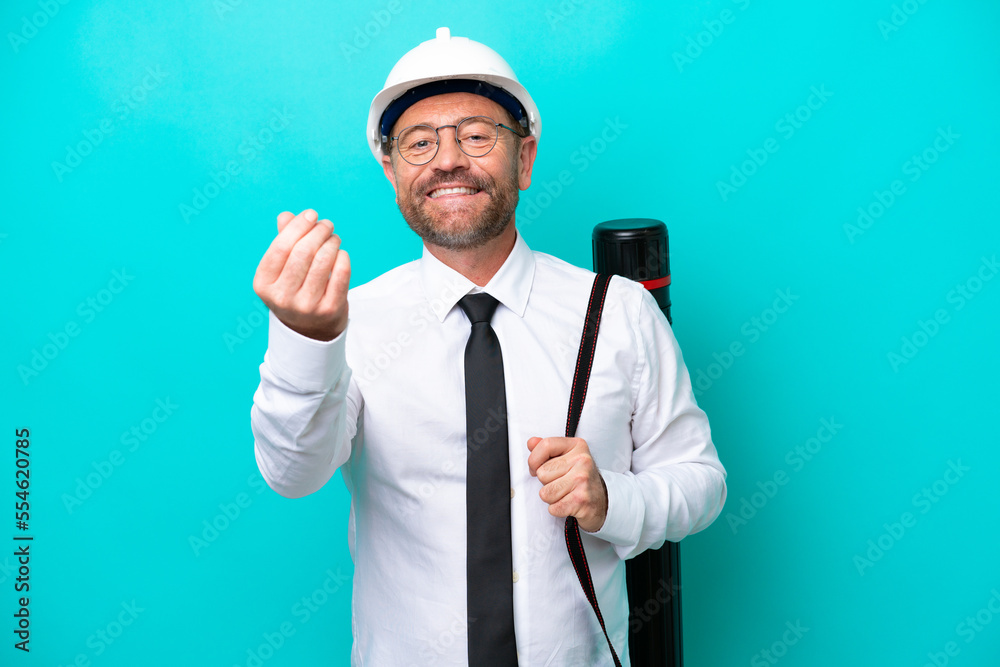 Wall mural Middle age architect man with helmet and holding blueprints isolated on blue background making money gesture