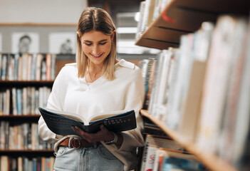 Happy, reading or student in library for books, educational knowledge or research for learning or assessment. School girl, college or university student studying for insight or scholarship on campus