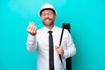 Middle age architect man with helmet and holding blueprints isolated on blue background making money gesture