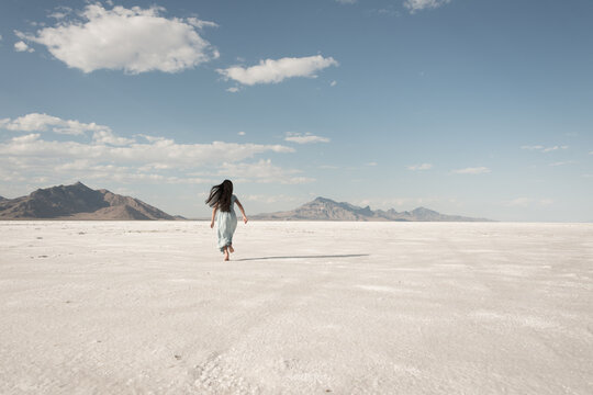 rear view of girl running in blue dress on white salt flats landscape in Utah, USA