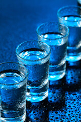 Wet glasses of vodka on dark blue background.