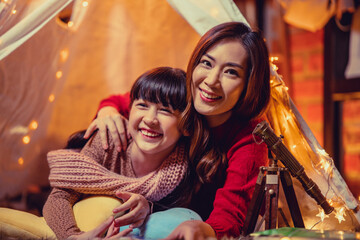 Happy mother and daughters reading a story book together in kids tent on Christmas eve. Celebrating Xmas at home.