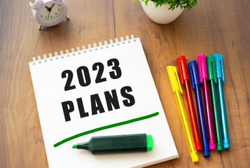 A notebook on a spring with the text 2023 PLANS lies on a brown wooden table.