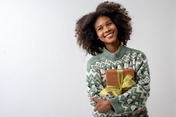 Portrait of young attractive african american woman with curly hair hugging gift box in studio on...