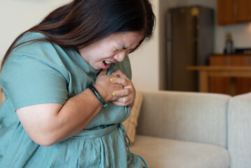 Indoor, close-up portrait of fat Asian woman sitting on sofa at home, holding chest, in pain, suffering from heart attack, unable to breathe.
Obesity, illness, health issues, heart failure concept.