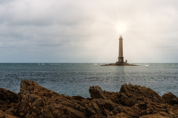 Fototapeta premium A scenic view of a lighthouse built on water near the shore with the sun shining brightly on top of it
