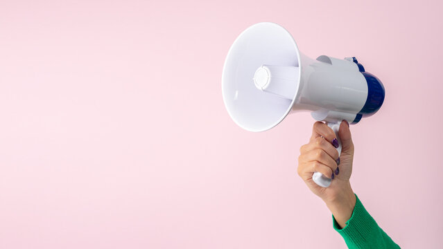 Woman hand with megaphone on pink background. Creative announcement concept.