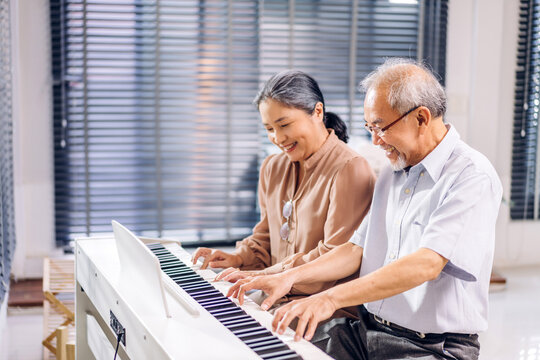 Portrait of enjoy happy love asian senior couple family having good time smiling and having fun play piano music lesson.Happy elderly husband and wife relax sitting on sofa at home