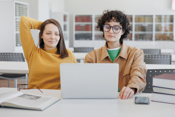 two female colleagues work on laptops in coworking office, library. online training webinar,...